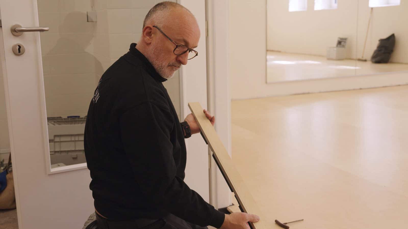 Gildas Février ajuste un seuil de porte dans une salle de danse terminée